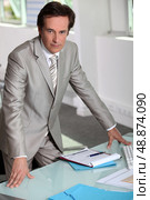 Man in a silver-grey suit purposefully standing by his desk. Стоковое фото, агентство Ingram Publishing / Фотобанк Лори