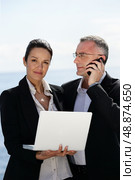 Businesswoman with laptop next to a collaborator on phone. Стоковое фото, агентство Ingram Publishing / Фотобанк Лори