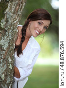 Smiling woman leaning out from behind a tree. Стоковое фото, агентство Ingram Publishing / Фотобанк Лори