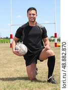 Man on  rugby pitch kneeling with ball under arm. Стоковое фото, агентство Ingram Publishing / Фотобанк Лори