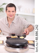 Man cooking raclette at the table. Стоковое фото, агентство Ingram Publishing / Фотобанк Лори