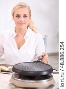 blonde woman in front of a heater preparing melted cheese, potatoes and cold meat (raclette) Стоковое фото, агентство Ingram Publishing / Фотобанк Лори