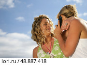 Two blond friends making a call whilst at the beach. Стоковое фото, агентство Ingram Publishing / Фотобанк Лори