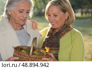 a mid age blonde woman and an older woman holding a wickerwork basket full of chestnuts. Стоковое фото, агентство Ingram Publishing / Фотобанк Лори