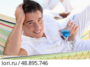 Young man enjoying a cocktail in a hammock. Стоковое фото, агентство Ingram Publishing / Фотобанк Лори