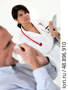 Doctor writing on a clipboard as her patient blows his nose. Стоковое фото, агентство Ingram Publishing / Фотобанк Лори