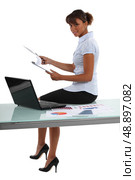 Businesswoman perched on a desk with statistics. Стоковое фото, агентство Ingram Publishing / Фотобанк Лори