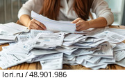 A woman is seated at a table cluttered with various papers and documents, appearing to work or study intently. Стоковое AI-изображение, AI-художник Данила Большаков / Фотобанк Лори