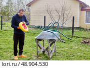 Inspecting replacement wheel before beginning mounting process to ensure proper fit and functionality for garden wheelbarrow repair outdoors. Стоковое фото, фотограф Владимир Григорьев / Фотобанк Лори