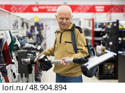 Senor man pensioner buying Upright Vacuum Cleaner in showroom of electrical appliance store. Стоковое фото, фотограф Татьяна Яцевич / Фотобанк Лори