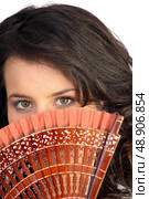 Closeup of a pretty woman hiding behind a fan. Стоковое фото, агентство Ingram Publishing / Фотобанк Лори
