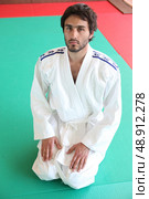 Adult male kneeling on mat in martial arts clothing. Стоковое фото, агентство Ingram Publishing / Фотобанк Лори