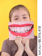 Girl holding an enlarged picture of her teeth in front of her mouth. Стоковое фото, агентство Ingram Publishing / Фотобанк Лори