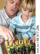 Young boy playing chess with his grandfather. Стоковое фото, агентство Ingram Publishing / Фотобанк Лори