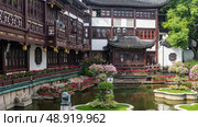 Beautiful Chinese park in the courtyard. Blooming bougainvilleas on flower beds in a pond. A building with balconies, terraces, and curved roof edges directly by the water. China. Shanghai. Yu Garden. Стоковое фото, фотограф Вера Ивановна Кубарева / Фотобанк Лори
