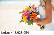 Bright wedding bouquet held by bride on sandy beach with ocean waves in background under clear blue sky. Стоковое AI-изображение, AI-художник Александр Калинин / Фотобанк Лори