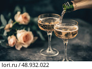 Champagne and red pink roses on a black concrete background. Copy space for text. Valentines drinks for for a pair of lovers. Bartender pours prosecco sparkling wine into glasses. Romance. Wedding Day. Стоковое AI-изображение, AI-художник Марина Демидюк / Фотобанк Лори