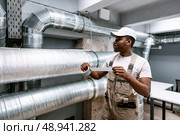 Worker inspects ductwork and applies tape in a modern building renovation project during the day. Стоковое фото, фотограф Сергей Толмачёв / Фотобанк Лори