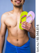 Happy young man holding pair of flip flops. Стоковое фото, агентство Ingram Publishing / Фотобанк Лори