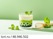 A sleek minimalist glass holds matcha bubble tea with creamy taro and black pearls. Mint green background elevates its aesthetic, with abstract shadows enhancing the elegant composition. Стоковое AI-изображение, AI-художник Nart / Фотобанк Лори