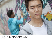 Portrait of serious young man with a cool attitude looking at the camera, young man spray painting in the background. Стоковое фото, агентство Ingram Publishing / Фотобанк Лори