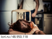 Crying woman in kitchen with abusive partner in the background. Стоковое фото, агентство Ingram Publishing / Фотобанк Лори