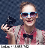 Smiling hipster girl with vintage camera. Trendy teenager in checkered red shirt and bow-tie and sunglasses. Стоковое фото, агентство Ingram Publishing / Фотобанк Лори