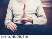 Young man is sitting on a sofa and holding a rotten carrot. Стоковое фото, агентство Ingram Publishing / Фотобанк Лори