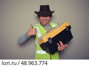 A cowboy builder with a big tool box is pulling silly faces and gesturing. Стоковое фото, агентство Ingram Publishing / Фотобанк Лори