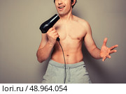 Athletic young man is holding a hair dryer and messing around with it. Стоковое фото, агентство Ingram Publishing / Фотобанк Лори