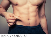 Fit young man pinching the fat on his stomach. Стоковое фото, агентство Ingram Publishing / Фотобанк Лори