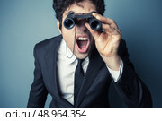 Young businessman is looking through binoculars and is surprised at what he sees. Стоковое фото, агентство Ingram Publishing / Фотобанк Лори