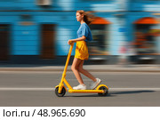 A woman is riding a yellow scooter down a street. Стоковое AI-изображение, AI-художник Ярославский Максим / Фотобанк Лори