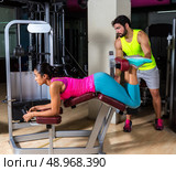 Lying hamstring curl machine girl with personal trainer man. Стоковое фото, агентство Ingram Publishing / Фотобанк Лори
