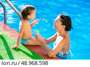 Baby girl blowing soap ballons with mother in swimming pool at summer vacation. Стоковое фото, агентство Ingram Publishing / Фотобанк Лори