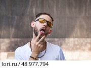 Tongue-tied Guy Wearing Shades Gestures With His Fingers Near a Textured Wall. Стоковое фото, фотограф Aleksandr Golubev / Фотобанк Лори