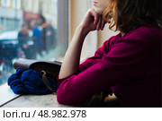 A young woman is sitting by a window and is looking out and day dreaming. Стоковое фото, агентство Ingram Publishing / Фотобанк Лори
