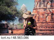 A young woman is drinking juice from a coconut near the ruins of an ancient buddhist temple. Стоковое фото, агентство Ingram Publishing / Фотобанк Лори