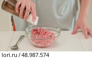 Person adds salt to raw ground meat in a glass bowl, preparing ingredients for cooking or meal preparation on a kitchen counter. Стоковое видео, видеограф Андрей Журавлев / Фотобанк Лори