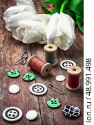 armful white tulip and buttons for clothing on deprecated wooden background.the image is tinted in vintage style. thread and buttons. Стоковое фото, агентство Ingram Publishing / Фотобанк Лори