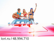 young group having fun on the beach playing guitar and dancing in a convertible car. Стоковое фото, агентство Ingram Publishing / Фотобанк Лори