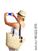 Blond tourist girl taking photos with smartphone white summer dress and basket bag. Стоковое фото, агентство Ingram Publishing / Фотобанк Лори