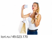 Blond shopaholic woman with bags selfie with smartphone on white background. Стоковое фото, агентство Ingram Publishing / Фотобанк Лори