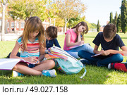 Group of little students sitting on the grass at school. Стоковое фото, агентство Ingram Publishing / Фотобанк Лори