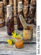 Elecampane tincture. infusion of inflorescences and roots of the medicinal plant Inula on the wooden table next mortar and pestle.Photo tinted. Стоковое фото, агентство Ingram Publishing / Фотобанк Лори
