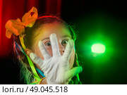 The little actress girl covered her face with a white glove and looks through her fingers. Stage light and child actor. Стоковое фото, фотограф Лазаренко Светлана / Фотобанк Лори