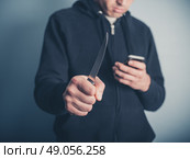 A young man is showing threatening behaviour by waving a knife whilst using a smartphone at the same time. Стоковое фото, агентство Ingram Publishing / Фотобанк Лори