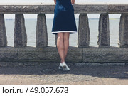 A young woman wearing a blue dress is standing by a wall with concrete balustrades on a promenade and is admiring the seaside on a sunny day. Стоковое фото, агентство Ingram Publishing / Фотобанк Лори