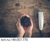 A male hand is holding some cut hair by a wooden table with a hair clipper. Стоковое фото, агентство Ingram Publishing / Фотобанк Лори