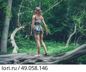 A barefoot young woman is standing on a fallen tree in the forest surrounded by ferns. Стоковое фото, агентство Ingram Publishing / Фотобанк Лори